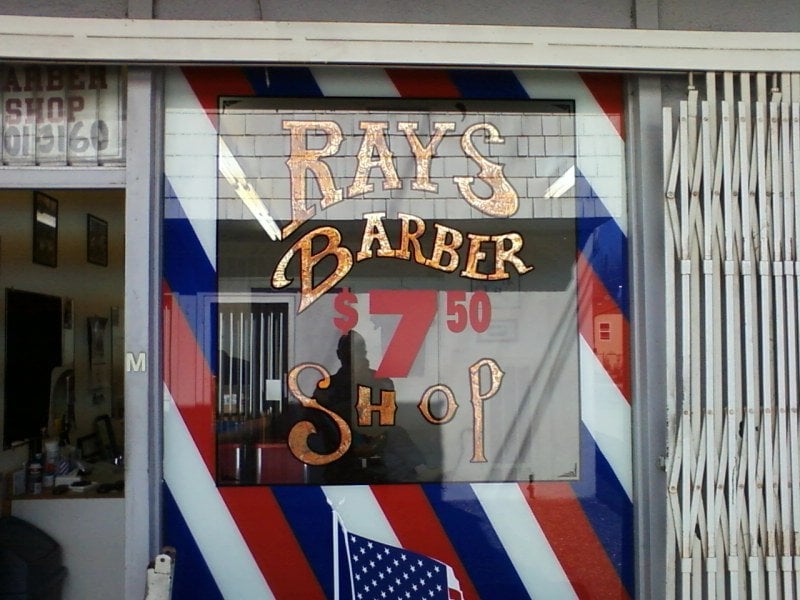 The storefront of Ray's Barber Shop on Beach Blvd, with hand-painted gold letters and barber pole stripes around the window